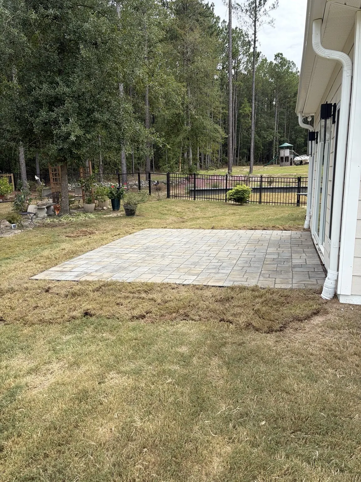 Paver patio built by RSL beside a house, with lawn around it and a fenced backyard beyond